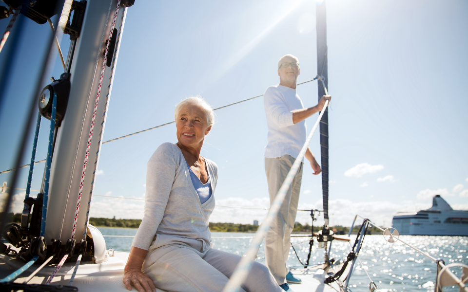 Glückliche Rentner segeln auf Yacht, strahlend in der Sonne. Sie scheinen einen erfolgreichen Anlageberater gehabt zu haben.
